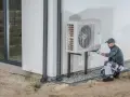 Instalator sprawdza pompę ciepła 3 fazową zamontowaną na ścianie budynku.