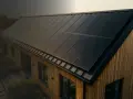 Nowoczesny dom z drewnianą elewacją i panele fotowoltaiczne na dachu. To wizualizacja produkcji energii z fotowoltaiki w poszczególnych miesiącach.