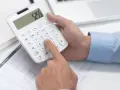 Ręce liczą na kalkulatorze, sprawdzając, czy nie nastąpiło przekroczenie mocy zamówionej. Na stole leżą dokumenty i tablet.