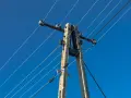 Słup energetyczny z przewodami na tle błękitnego nieba. Zastanawiasz się, ile wynosi odszkodowanie za słupy energetyczne na działce?