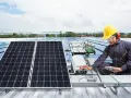 Technik w żółtym kasku sprawdza instalację solar edge na dachu. Panele słoneczne błyszczą w słońcu.