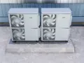 Dwie jednostki zewnętrzne pomp ciepła, idealne do domu 100m2, stoją na betonowym postumencie.
