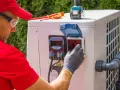 Technik w czerwonej koszulce i czapce reguluje pokrętło na pompie ciepła. Czy pompę ciepła można wyłączyć? Tak, za pomocą tego panelu.