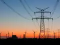 Zachód słońca nad krajobrazem z wiatrakami i liniami wysokiego napięcia. Tauron zapewnia energię w sieci.