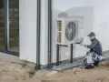 Technik wykonuje protokół uruchomienia pompy ciepła, sprawdzając instalację przy ścianie budynku.