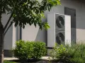 Nowoczesna pompa ciepła 3 5 kw, dyskretnie umieszczona przy ścianie domu, otoczona zielenią, zapewnia ekologiczne ogrzewanie.