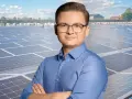 Mężczyzna w okularach na tle farmy fotowoltaicznej. Szanuj energię, nie daj się oszustom.