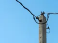 Betonowy słup energetyczny z przewodami na tle błękitnego nieba. Zastanawiasz się, ile za słup energetyczny na działce?