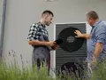 Technik z tabletem i klient przy pompie ciepła. Rozmawiają o ekonomicznym ustawieniu pompy ciepła, by zapewnić optymalne ogrzewanie domu.
