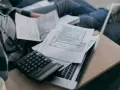 Osoba przegląda dokumenty podatkowe, kalkulator i laptop. Zastanawia się, do kiedy obowiązuje tarcza na prąd.
