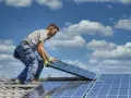 Instalator montuje panele fotowoltaiczne na dachu. Optymalne ustawienie paneli wschód-zachód zapewnia maksymalne wykorzystanie energii słonecznej.