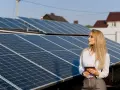 Kobieta z tabletem analizuje instalację fotowoltaiczną. Czy panele fotowoltaiczne są szkodliwe? Analiza danych na tle paneli.