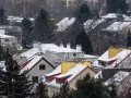 Zimowy krajobraz z ośnieżonymi dachami domów. Dym z komina sugeruje, że węglem pali się nawet w cieplejsze dni, choć warto wiedzieć, do kiedy można palić węglem.