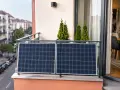 Mini elektrownia słoneczna na balkonie, z widokiem na ulicę i kamienice. Dwa panele fotowoltaiczne łapią promienie słońca.