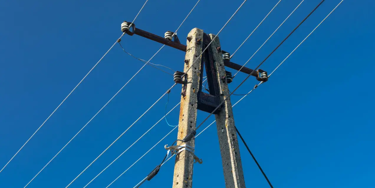 Słup energetyczny z przewodami na tle błękitnego nieba. Zastanawiasz się, ile wynosi odszkodowanie za słupy energetyczne na działce?