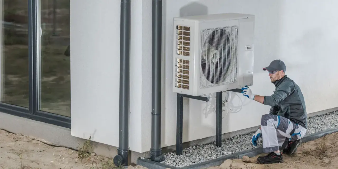 Technik wykonuje protokół uruchomienia pompy ciepła, sprawdzając instalację przy ścianie budynku.