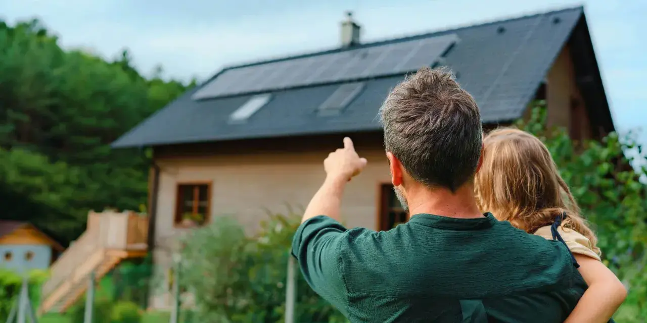 Ojciec z dzieckiem patrzą na dom z panelami fotowoltaicznymi. Zastanawiają się, fotowoltaika 6 kw ile wyprodukuje energii.