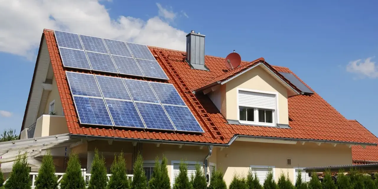 Dom z czerwoną dachówką i panelami fotowoltaicznymi. Mikroinstalacja PV na dachu zapewnia czystą energię.