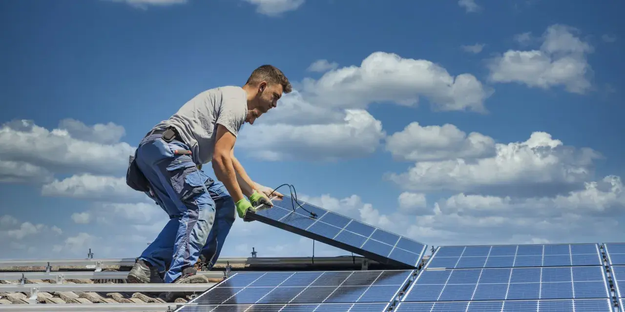 Instalator montuje panele fotowoltaiczne na dachu. Optymalne ustawienie paneli wschód-zachód zapewnia maksymalne wykorzystanie energii słonecznej.