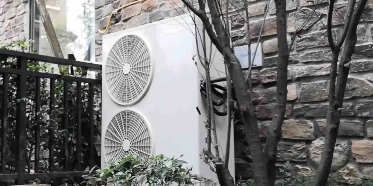 Dwa wentylatory jednostki zewnętrznej klimatyzatora sprsun, zamontowane na kamiennej ścianie, otoczone zielenią i gałęziami drzew.