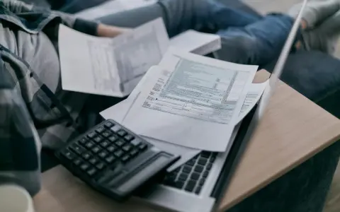 Osoba przegląda dokumenty podatkowe, kalkulator i laptop. Zastanawia się, do kiedy obowiązuje tarcza na prąd.