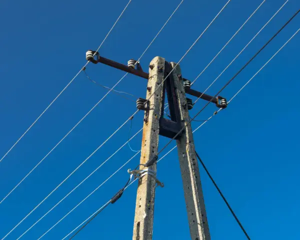 Słup energetyczny z przewodami na tle błękitnego nieba. Zastanawiasz się, ile wynosi odszkodowanie za słupy energetyczne na działce?