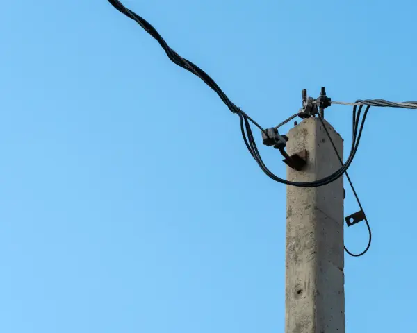 Betonowy słup energetyczny z przewodami na tle błękitnego nieba. Zastanawiasz się, ile za słup energetyczny na działce?