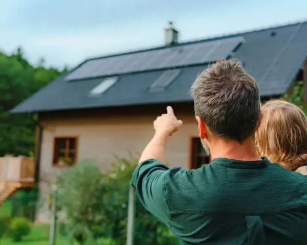 Ojciec z dzieckiem patrzą na dom z panelami fotowoltaicznymi. Zastanawiają się, fotowoltaika 6 kw ile wyprodukuje energii.