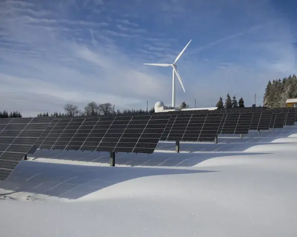 Panele fotowoltaiczne i wiatrak na tle zimowego krajobrazu. Rozliczenie z PGE za energię odnawialną.