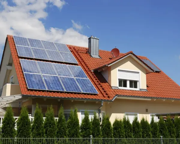 Dom z czerwoną dachówką i panelami fotowoltaicznymi. Mikroinstalacja PV na dachu zapewnia czystą energię.
