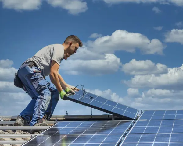 Instalator montuje panele fotowoltaiczne na dachu. Optymalne ustawienie paneli wschód-zachód zapewnia maksymalne wykorzystanie energii słonecznej.