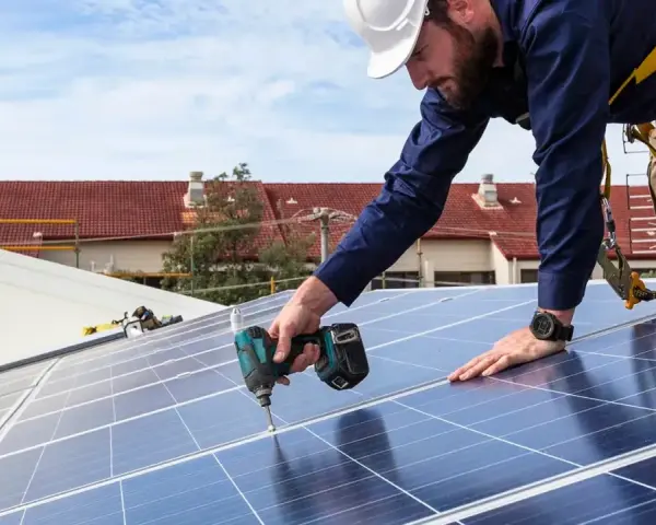 Instalator fotowoltaiki montuje panele na dachu. Szkolenie dla przyszłych fachowców.