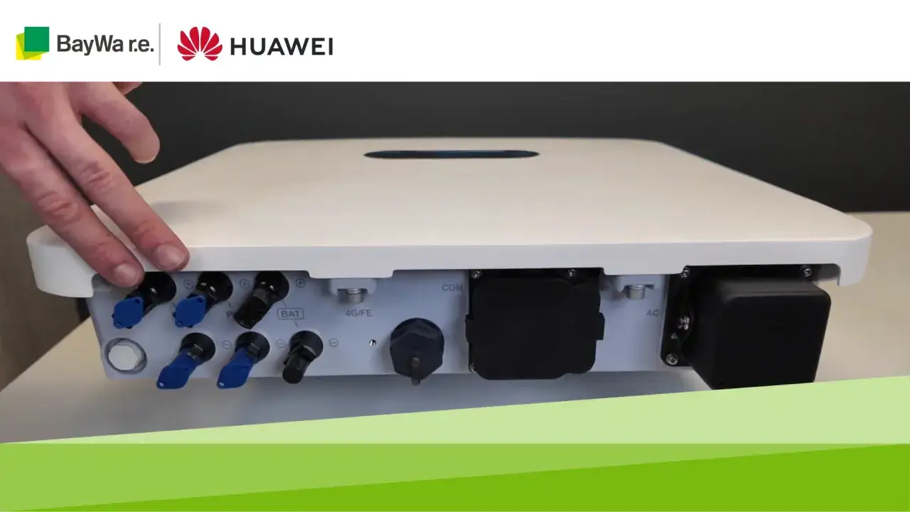 Dłoń wskazuje na złącza falownika Huawei 6kW. Widoczne są porty DC, AC, COM i 4G/FE.