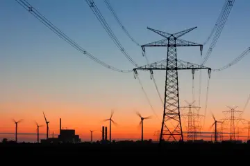 Zachód słońca nad krajobrazem z wiatrakami i liniami wysokiego napięcia. Tauron zapewnia energię w sieci.