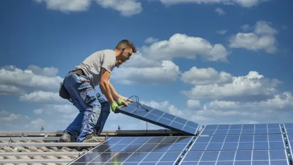 Instalator montuje panele fotowoltaiczne na dachu. Optymalne ustawienie paneli wschód-zachód zapewnia maksymalne wykorzystanie energii słonecznej.
